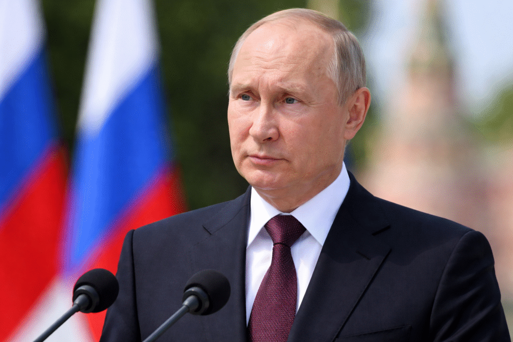 Russian President Vladimir Putin speaking at a formal ceremony, standing at microphones with Russian flags and the Kremlin blurred in the background.