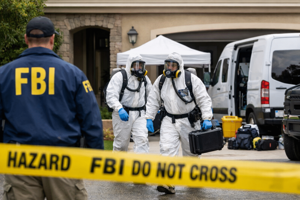 FBI hazmat team members in protective suits approach a suburban home in a gated Orange County community while an agent stands near a secured perimeter.