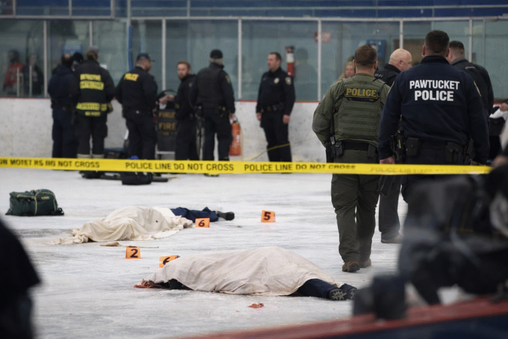Law enforcement officers and investigators inside an indoor ice rink securing a shooting scene, with covered victims on the ice and police tape visible in the foreground.