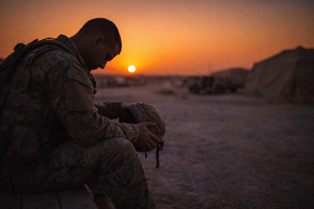 A solitary soldier sitting at a military base during sunset, reflecting a mood of fatigue and uncertainty related to deployment.