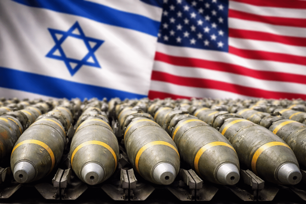 Rows of military bombs lined up in the foreground, with blurred United States and Israeli flags displayed side by side in the background.