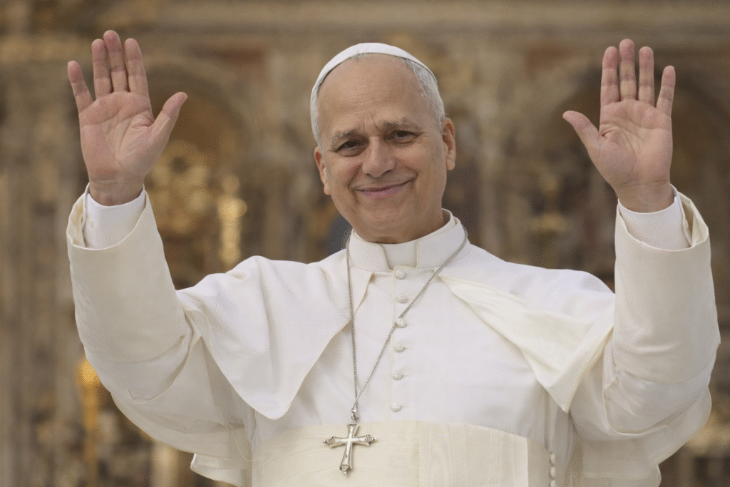 Pope in white papal attire raising both hands in a welcoming gesture inside a softly lit church interior.
