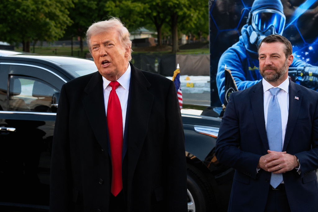 Donald Trump speaking outdoors beside a suited official near black vehicles and a large futuristic display during a public event.