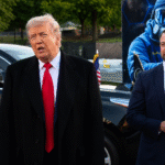Donald Trump speaking outdoors beside a suited official near black vehicles and a large futuristic display during a public event.