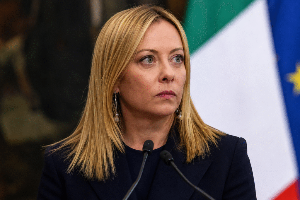 Italian Prime Minister Giorgia Meloni speaks at a podium during an official event with Italian and European Union flags visible in the background.
