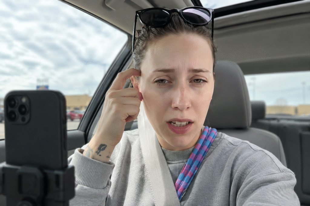 Young woman sitting inside a parked car recording a social media video on a smartphone, with sunglasses on her head and an expressive facial gesture while speaking.